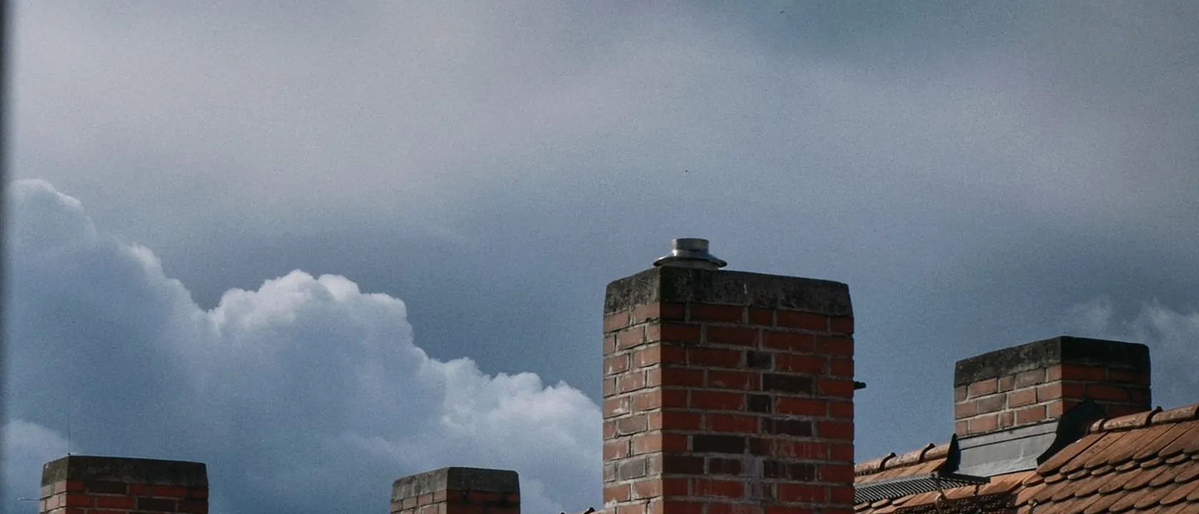 Cheminées en brique sur une toiture en tuile, sous un ciel nuageux