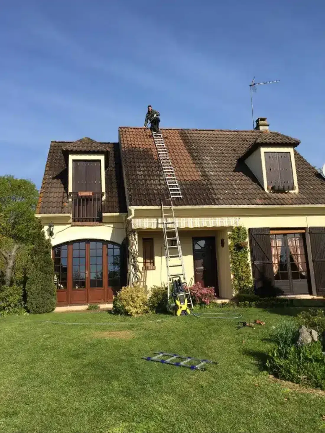 Couvreur sur le faîtage d'un pavillon, échelle appuyée sur la toiture
